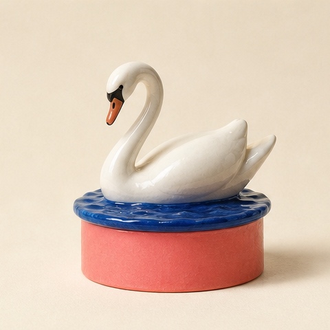 A white ceramic swan circling cobalt water on a coral drum.